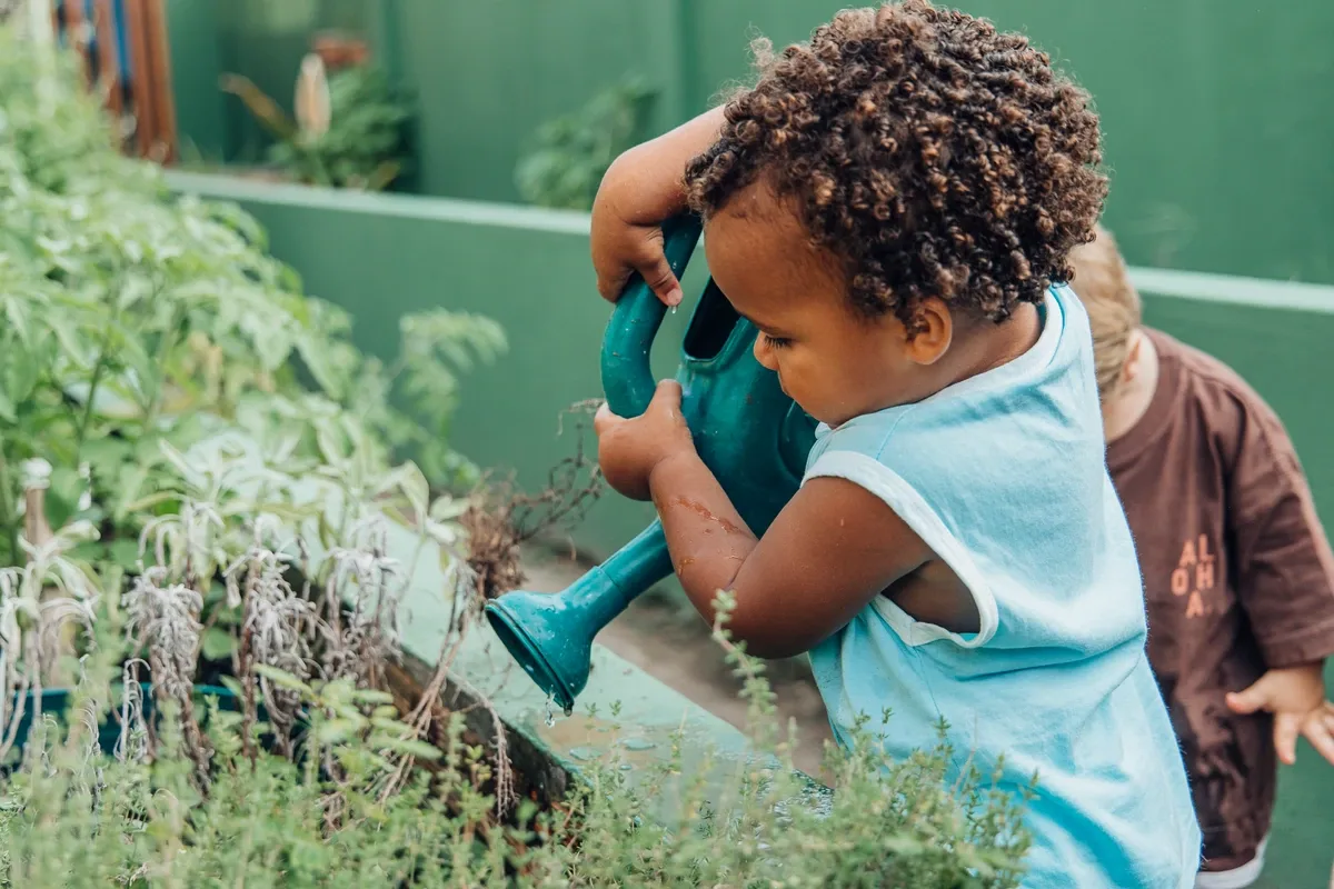 Criança rega plantas com um regador.