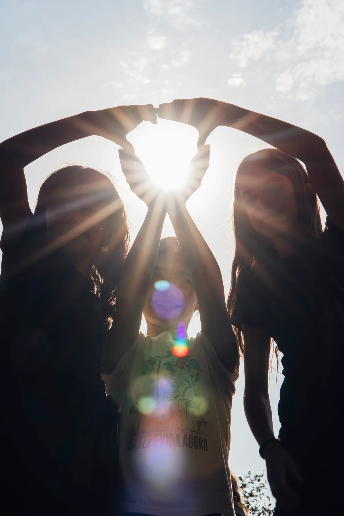 Crianças aproximam as mãos sob a luz do sol.