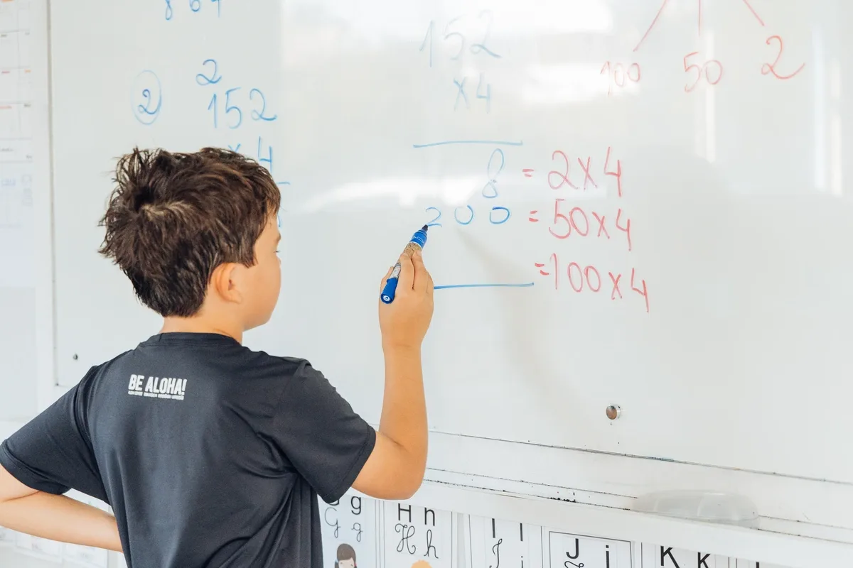 Aluno escreve números e operações no quadro.